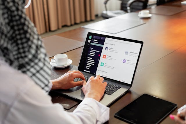 Person sitting at a table typing on a laptop next to a tea cup